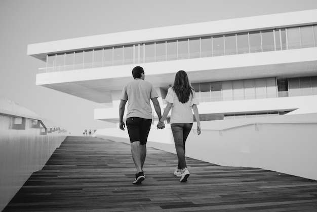 A stylish young man is holding hands with his brunette girlfriend in the port