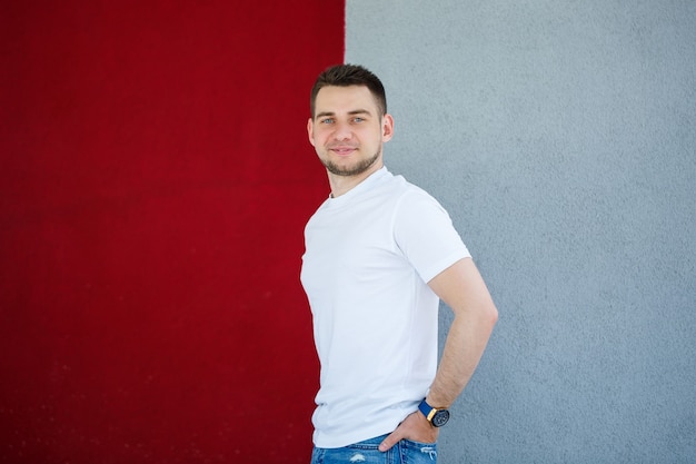 Stylish young man, a man dressed in a white blank t-shirt standing on a gray and red wall background. Urban style of clothes, modern fashionable image. Men's fashion