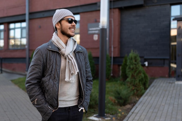 Stylish young man in sunglasses and hat with scarf outside