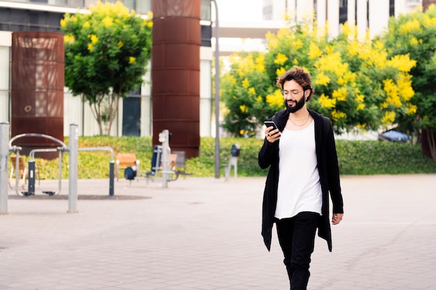 Stylish young man walking using a phone at city