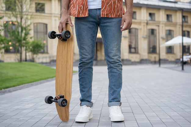 Stylish young man wearing casual clothing, white shoes holding skateboard, standing in park