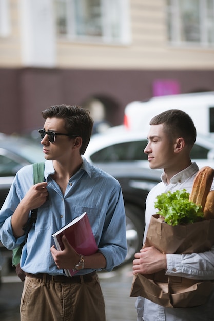 Stylish young men shopping. Hipster youth. Healthy food for two males, modern pedestrians on street