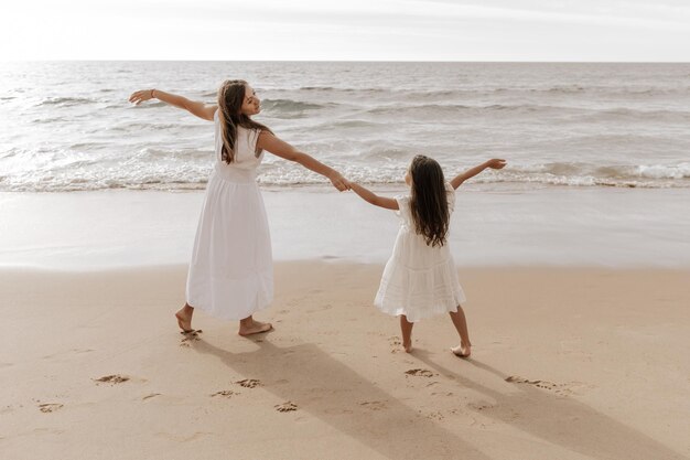 stylish young mother with little daughter dancing on sandy seashore