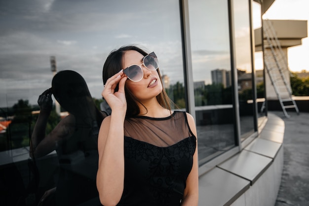 Stylish young and sexy girl posing in front of a business center in black. Fashion and style