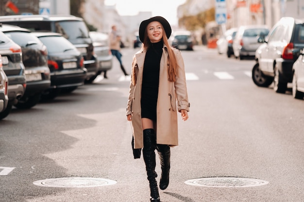 Stylish young woman in a beige coat in a black hat on a city street. Women's street fashion. Autumn clothing.Urban style.