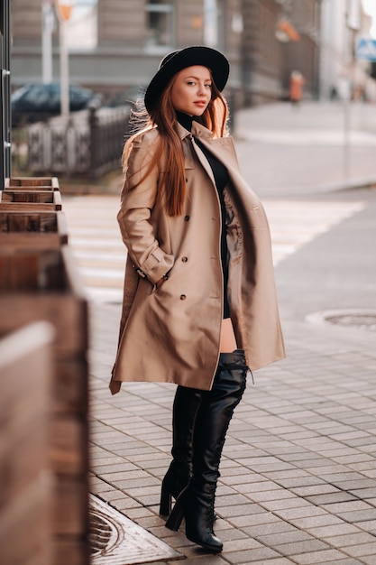 街の通りに黒い帽子をかぶったベージュのコートを着たスタイリッシュな若い女性。女性のストリートファッション。秋の服。アーバンスタイル。