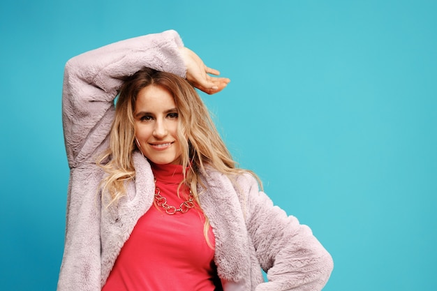 Stylish young woman dancer in pink coat posing against blue background