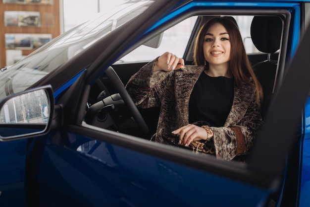 A stylish young woman is choosing a new car in a car store