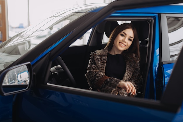 A stylish young woman is choosing a new car in a car store