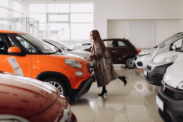 A stylish young woman is choosing a new car in a car store