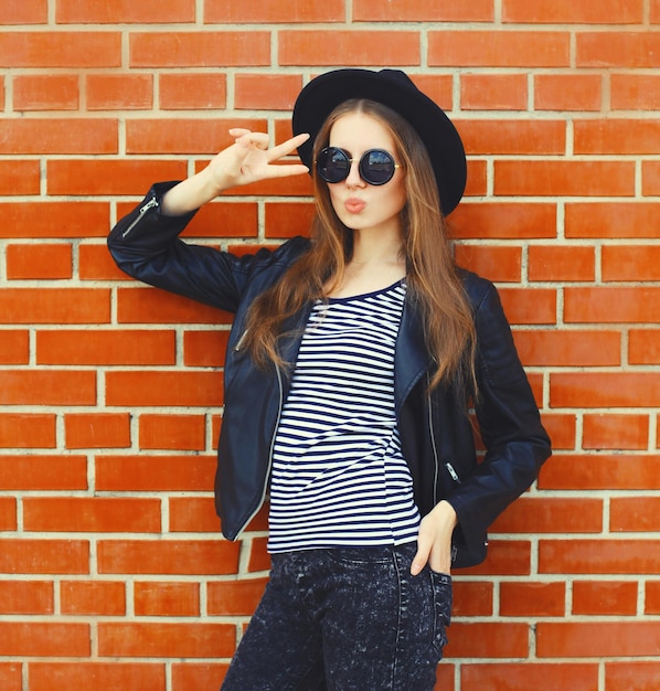 stylish young woman model wearing black round hat leather jacket in rock style on city street