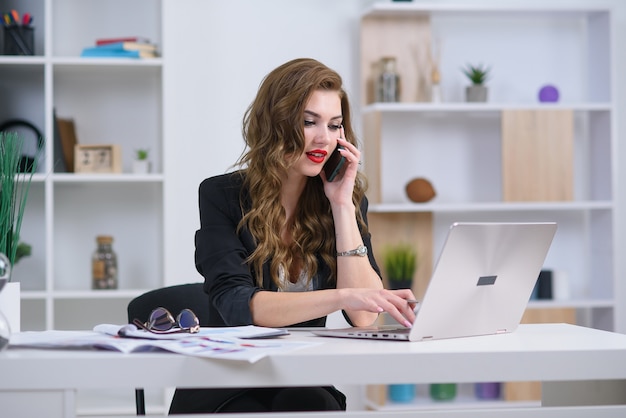 Stylish young woman in official clothes has mobile conversation with business partner in her office