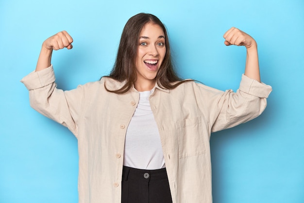 Stylish young woman in an overshirt showing strength gesture with arms symbol of feminine power