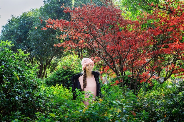 Stylish young woman in pink knitted hat standing in the park