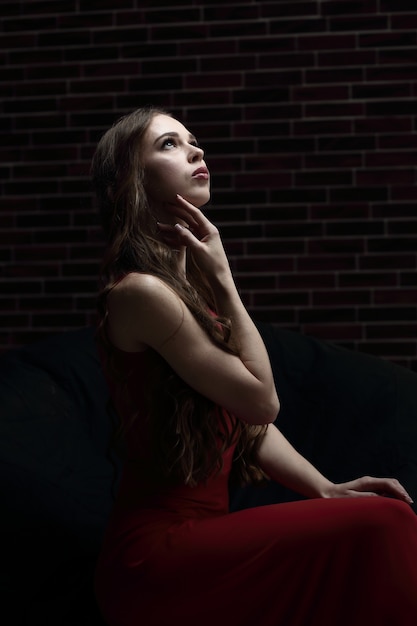 стильная молодая женщина в красном платье, сидя в кресле.