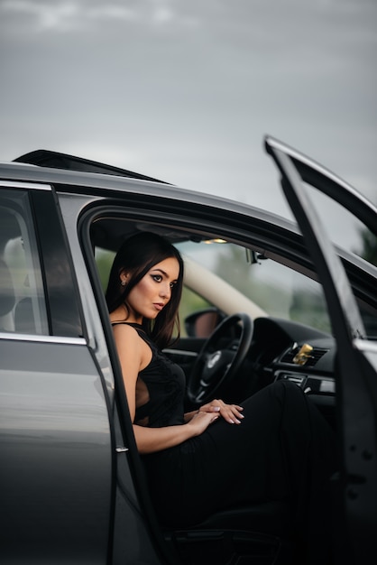 Foto giovane donna alla moda che si siede in un'automobile del business class in un vestito nero