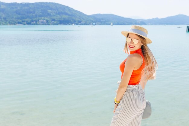 Stylish young woman smiles lake and mountains girl in sunglasses and boater