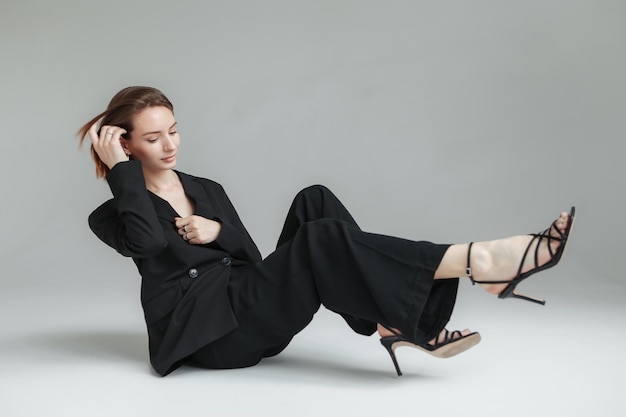 Stylish young woman in suit on gray background