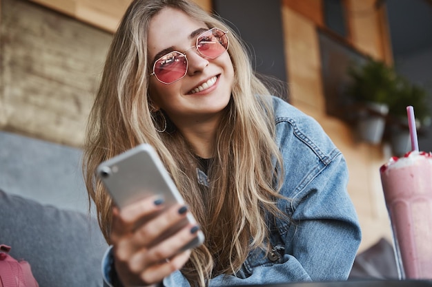 Stylish young woman in sunglasses sitting outdoor cafe and using