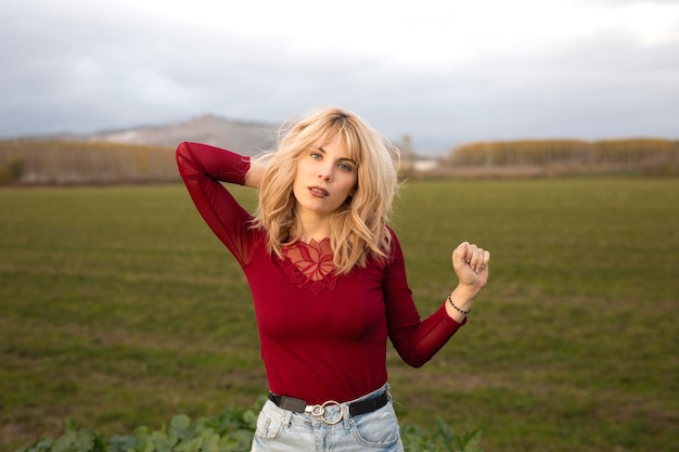 Stylish young woman touching blond hair in field