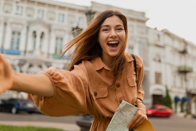 ヨーロッパを旅するスタイリッシュな若い女性は、春の流行のドレスとアクセサリーを身に着けて幸せに笑って楽しんでいます