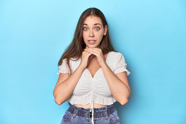 Stylish young woman in white blouse praying for luck amazed and opening mouth looking to front