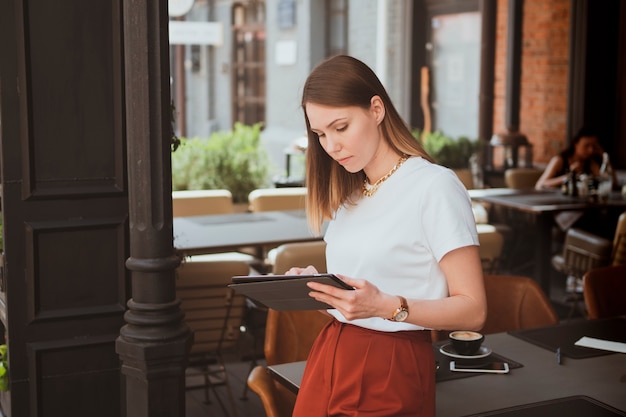 Photo stylish young woman with digital tablet working in street cafe