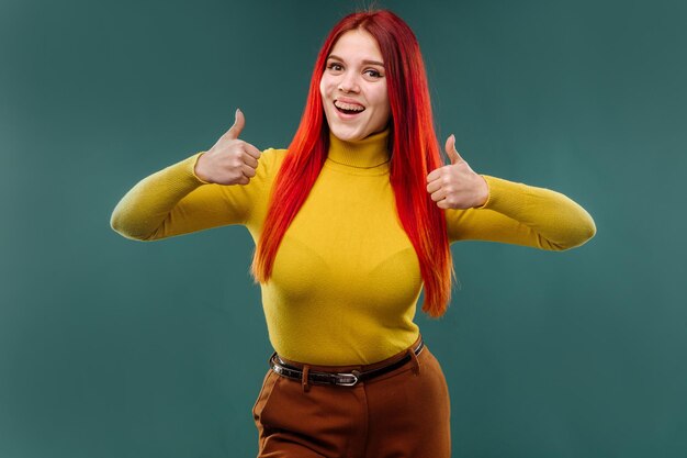 Stylish young woman with long red hair wearing yellow sweater posing emotionaly on studio background