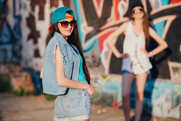 Stylish young women in caps at graffiti wall