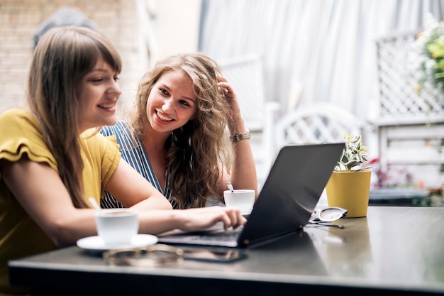 Stylish young women having friendly meeting with cups of coffee while using the laptop