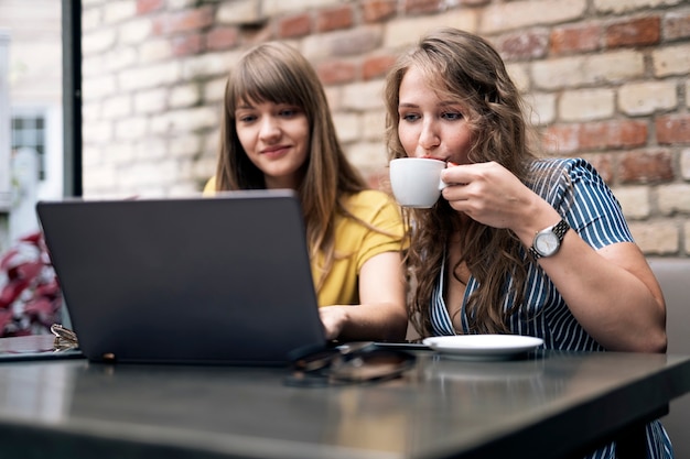 Stylish young women having friendly meeting with cups of coffee while using the laptop