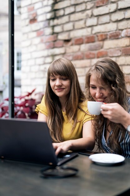 Stylish young women having friendly meeting with cups of coffee while using the laptop