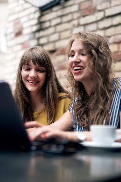 Stylish young women having friendly meeting with cups of coffee while using the laptop