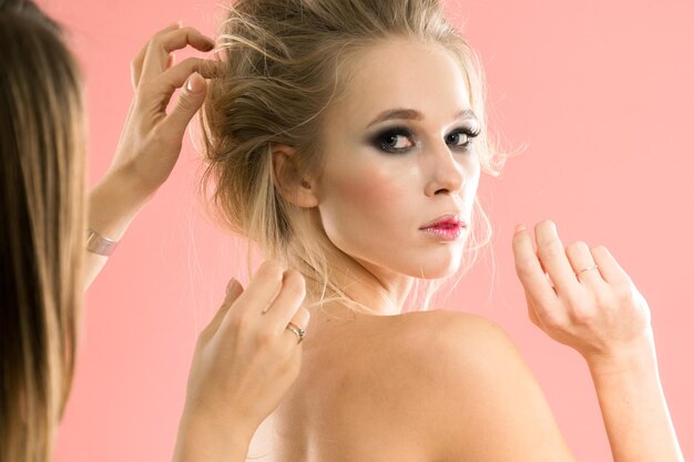 Stylist corrects hair girl in the studio on a pink background