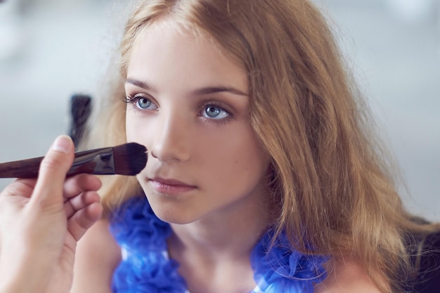 Stylist die de make-up doet voor een mooi klein meisjesmodel. Close-upbeeld.