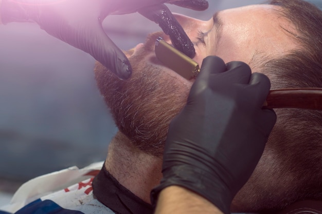 The stylist makes a model beard to a young guy in a beauty salon.