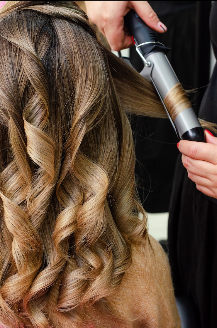 Photo stylist making a hairdo with hair curler. beauty salon concept