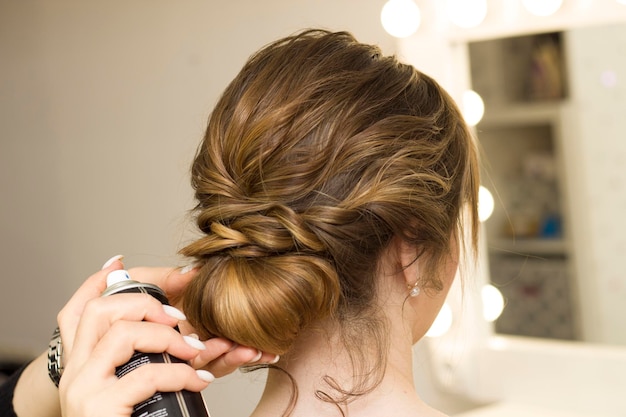 The stylist performs the hairstyle, hair styling in the salon. Splashes hairspray.