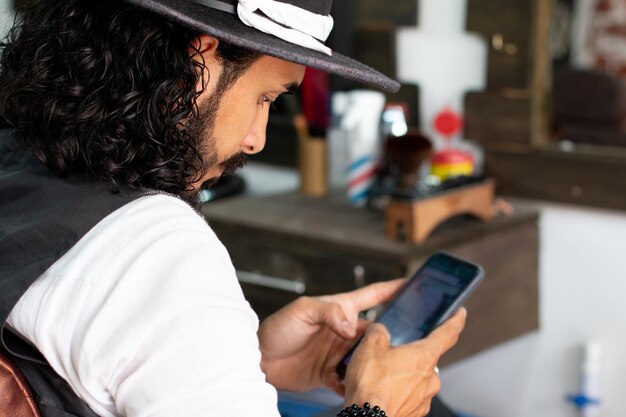 Stylist sitting in his barbershop chair using his smart phone while chatting