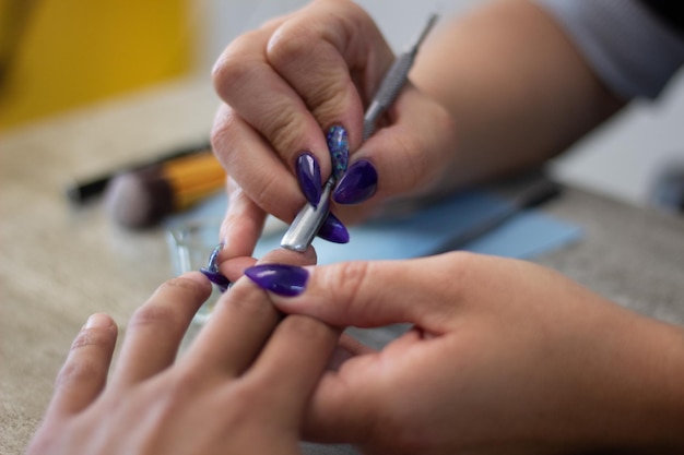 Stylist with blue artificial nails performing a manicure for a client