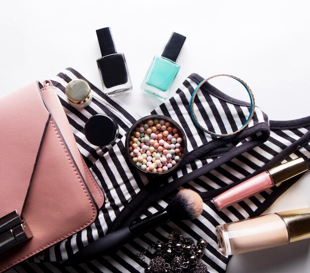 Stylized feminine flatlay with glasses foundation lip gloss powder brush handbag striped shirt