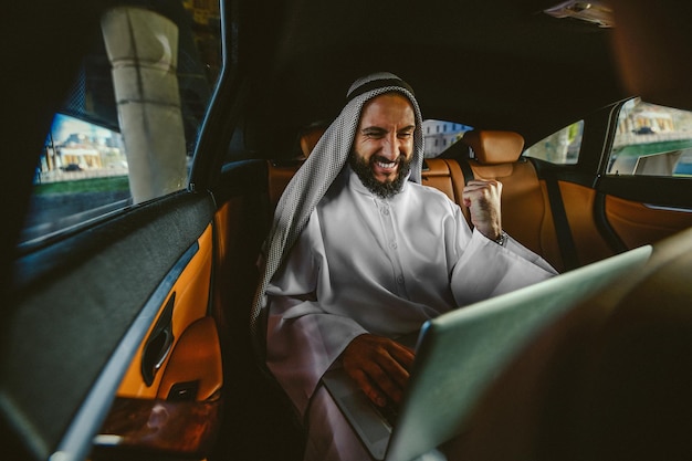 A suadi businessman working on a laptop in a car