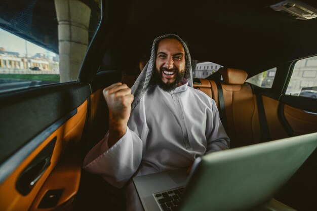 A suadi businessman working on a laptop in a car