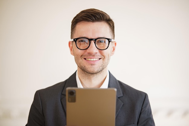 Photo a suave businessman with a pleasant smile holds a tablet his sharp attire and stylish eyeglasses