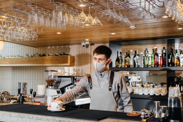 Submission of a Barista in a mask of delicious organic coffee in modern cafe during the pandemic.