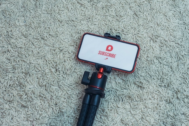 Subscribe to the Internet channel on the smartphone display on a flexible tripod against the background of the carpet.