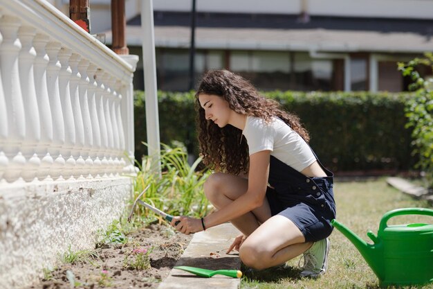 Photo suburban life young woman with curly hair working in the yard planting flowers in fruitful soil in the garden