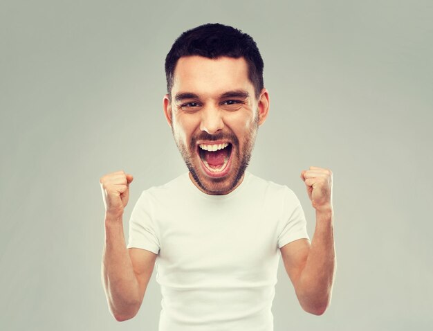 succes, gebaar en mensen emotie concept - jonge man vieren overwinning en schreeuwen over grijze achtergrond (grappige cartoon stijl personage met groot hoofd)