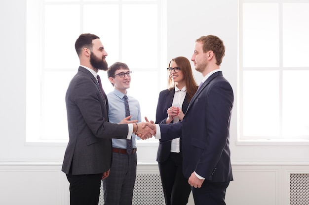 Succesful business people in office, young managers male and female unite hands for teamwork and cooperation after long discussion. White background with windows. Copy space