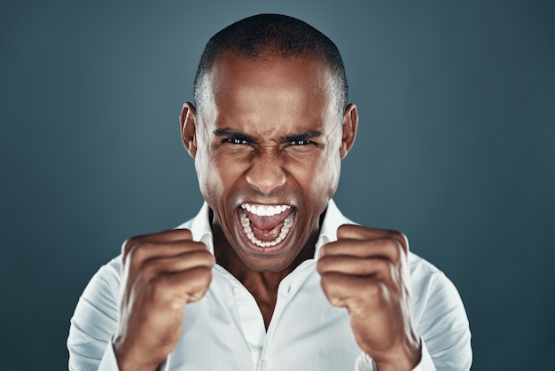 Success achieved. Handsome young African man in shirt gesturing and shouting while standing against grey background